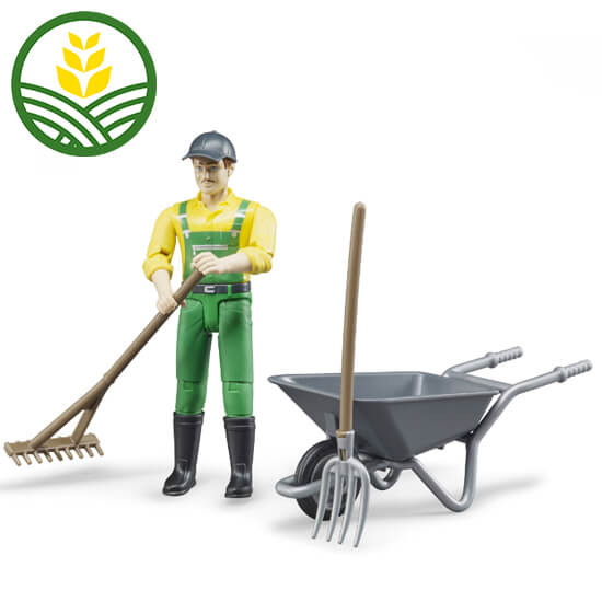 A toy male figure dressed in yellow and green John Deere overalls with a rake, pitch fork and wheelbarrow 
